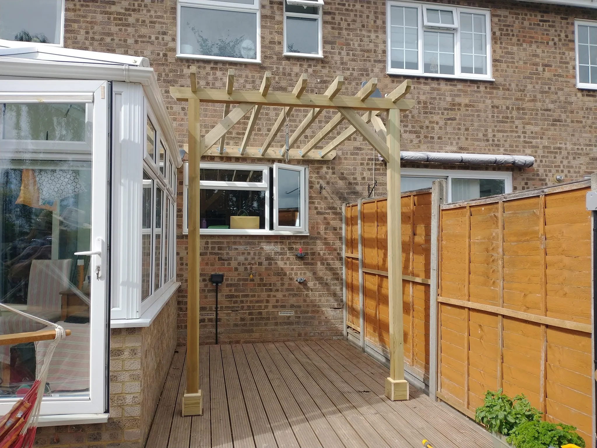 Bespoke timber pergola built over a narrow deck between a conservatory and garden fence.