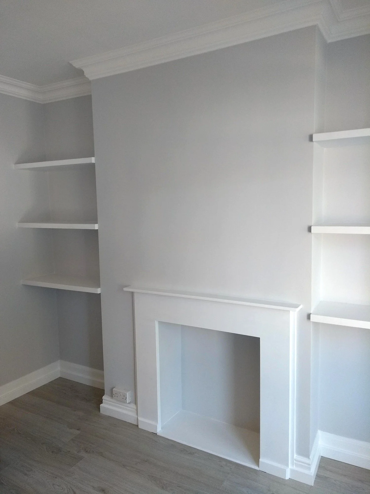Refurbished fireplace with a white surround, fitted shelves in both alcoves and soft grey walls.