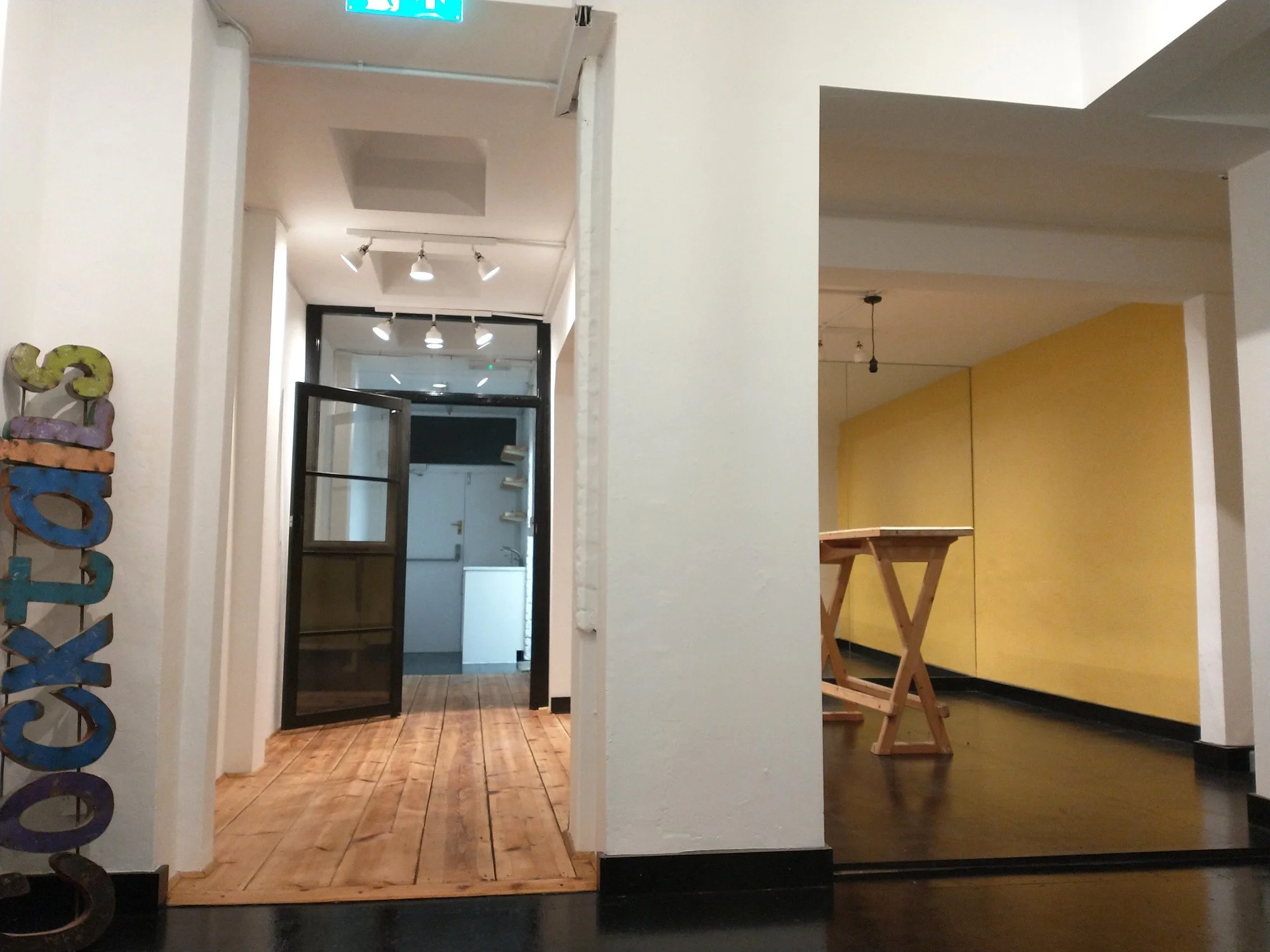 Refurbished shop interior with white walls, timber flooring and an open black-framed glazed door beside a yellow-walled area.