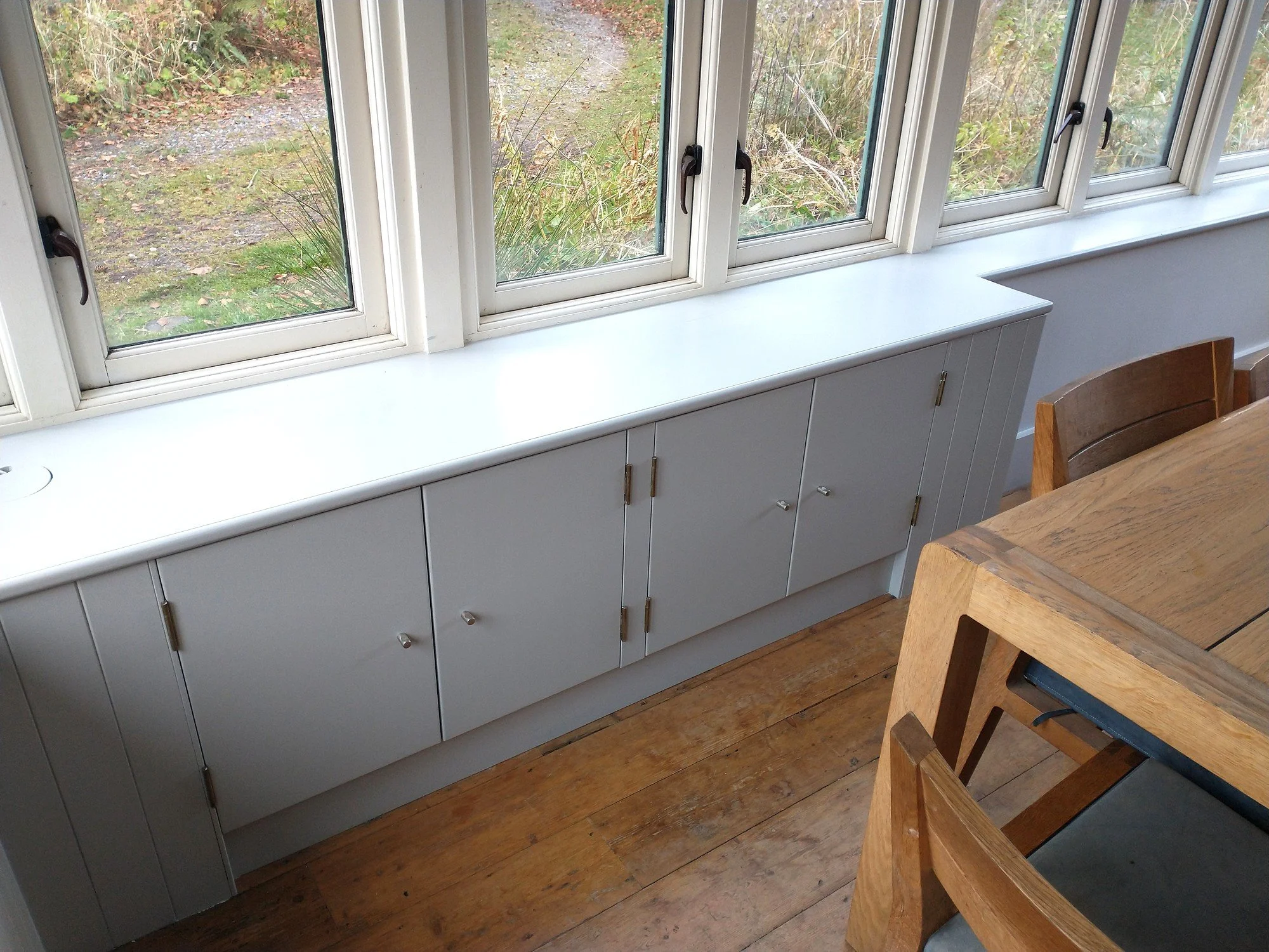 Freshly painted pale grey cupboards beneath white window frames and a matching painted sill.