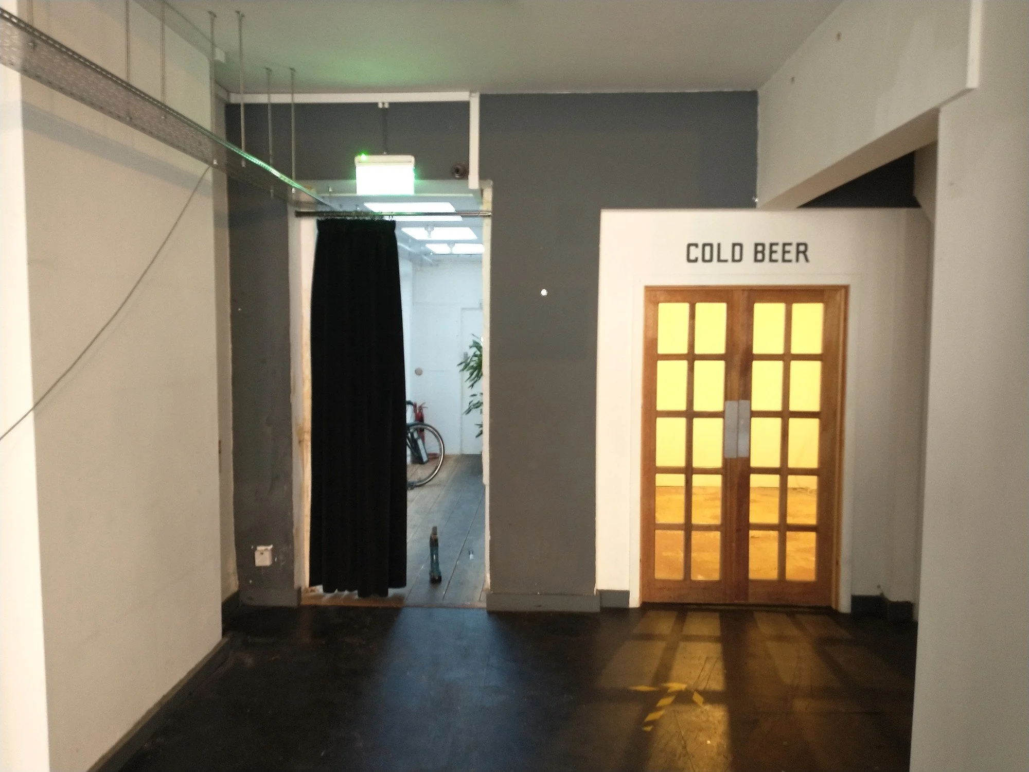 Shop interior before refurbishment, with dark flooring, a curtained doorway and glazed wooden double doors.