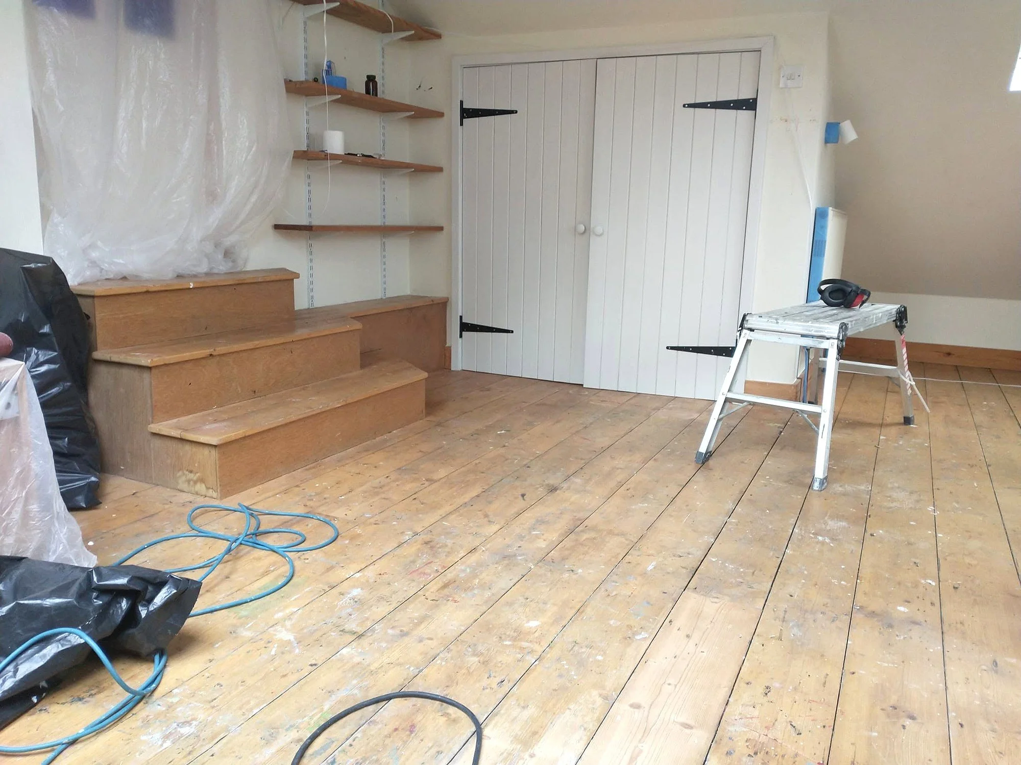 Mezzanine during decorating, with bare timber steps, wooden shelves, protective sheeting and a work platform.