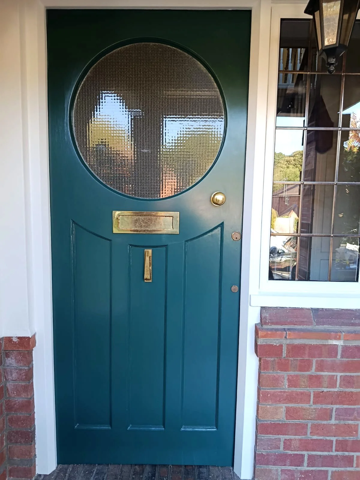 Freshly painted teal front door with a circular textured-glass window, brass fittings and a white frame.