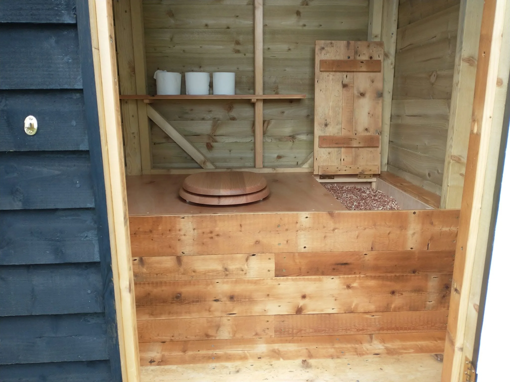 Timber-lined composting toilet interior with a shelf holding toilet rolls.