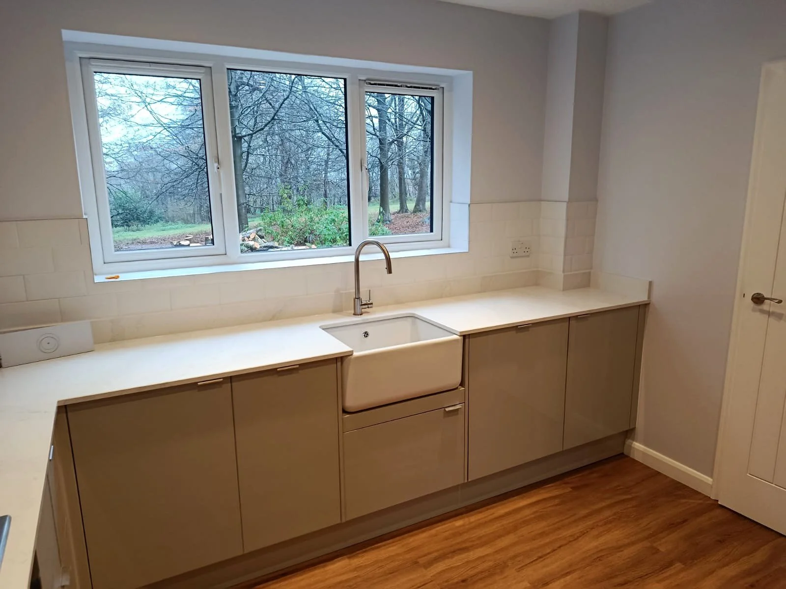 Refurbished kitchen with a white apron-front sink beneath the window, neutral cabinets and white worktops.