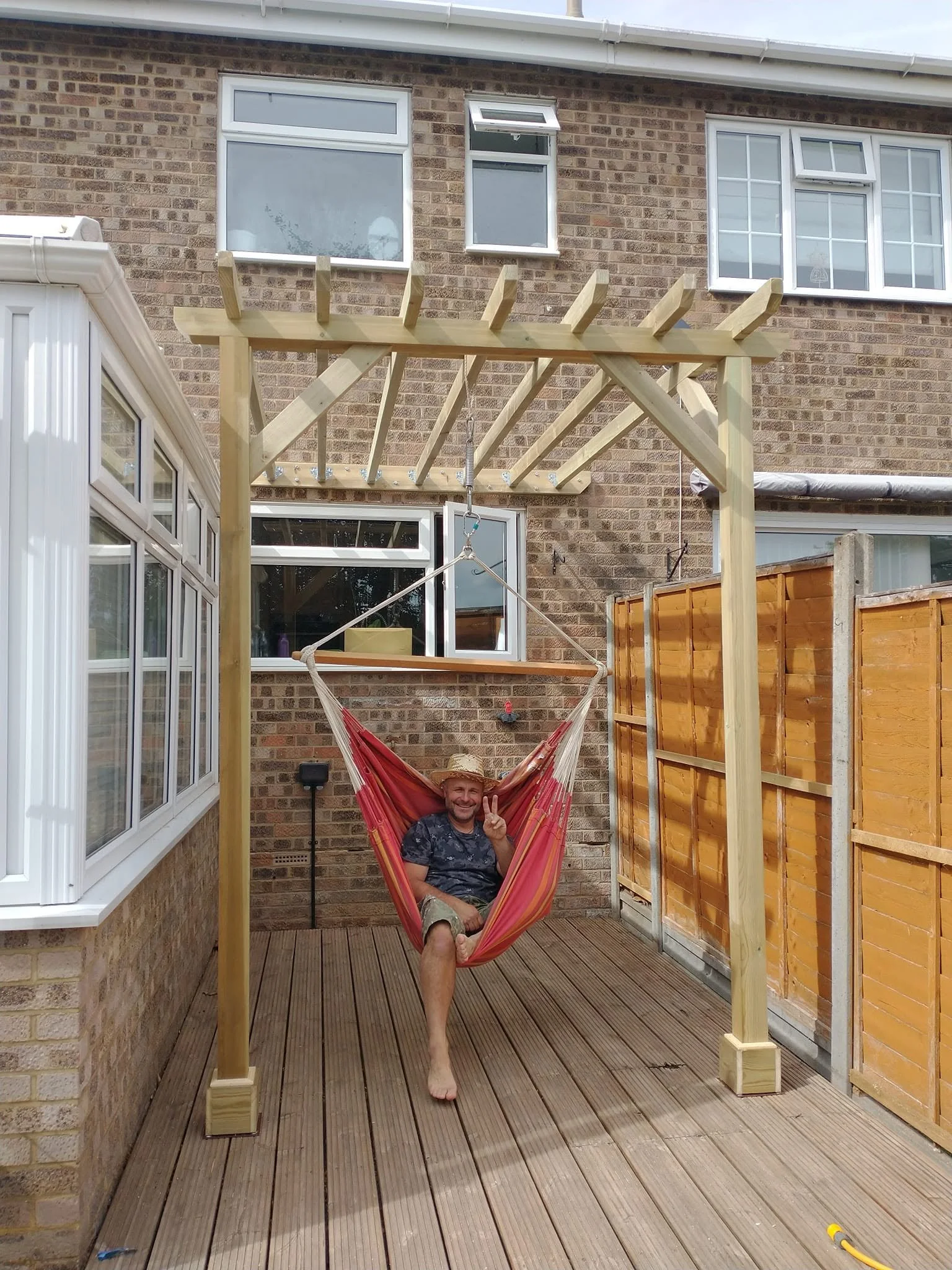 Completed timber pergola with a person relaxing in a red hanging chair beneath the beams.