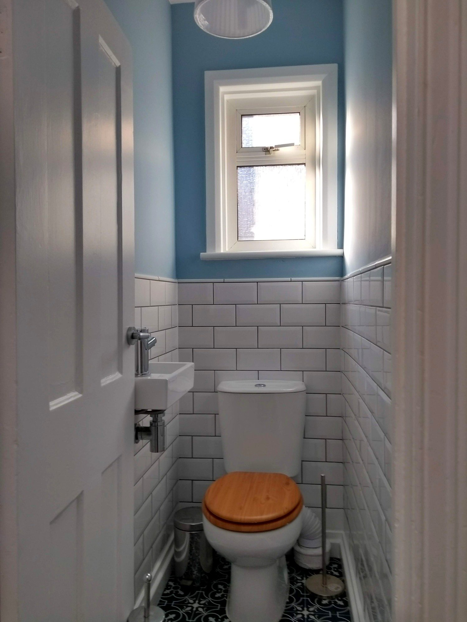 Refurbished toilet with blue walls, white metro tiles, a compact hand basin and black-and-white patterned flooring.