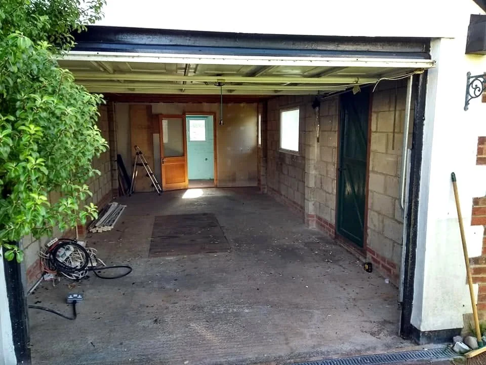 Garage before conversion, with exposed block walls, a bare concrete floor and an open up-and-over door.