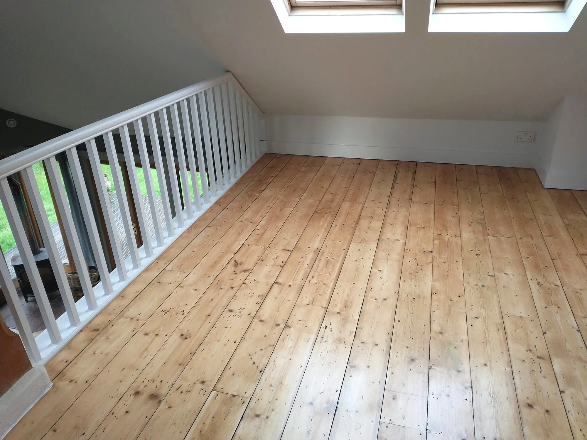 White painted mezzanine balustrade beside timber floorboards, with pale sloping walls and roof windows above.