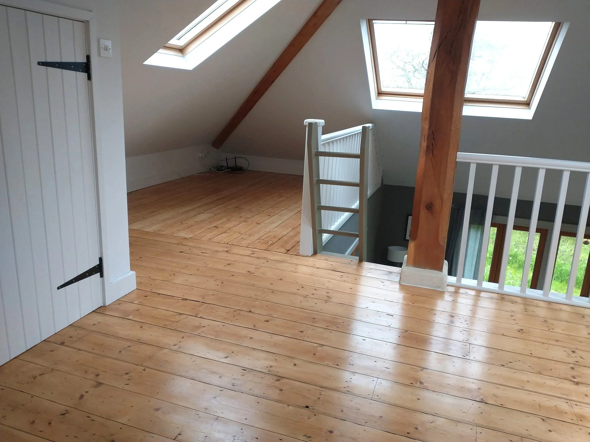 Painted mezzanine with white stair rails and woodwork, exposed timber beams and natural floorboards beneath roof windows.