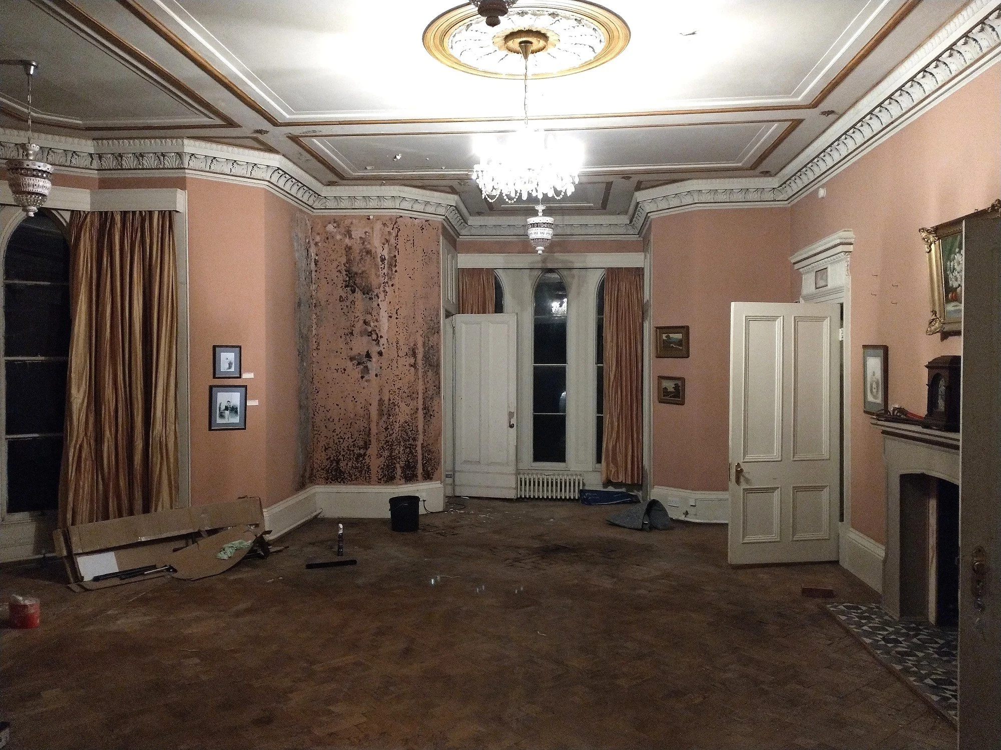 Period reception room during preparation, with partially stripped walls, an ornate ceiling and white woodwork.