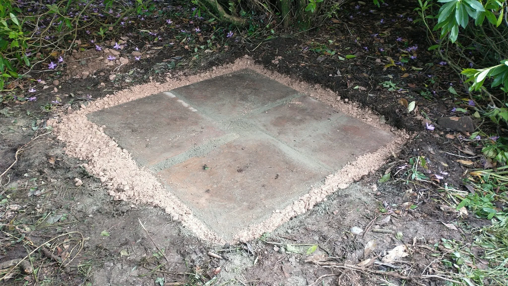Paving slab base prepared for a garden composting toilet among trees and shrubs.