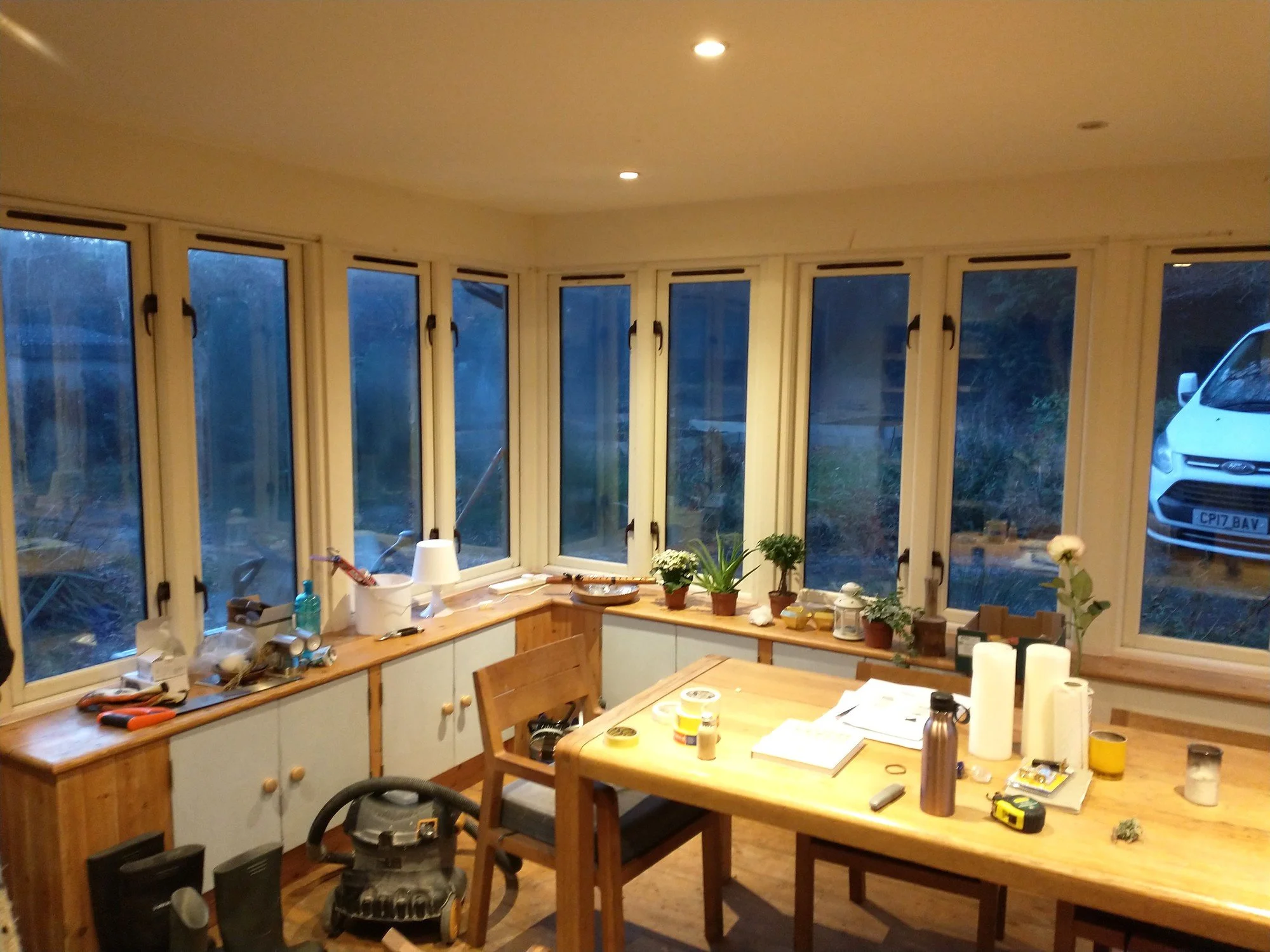 Window-side cupboards before painting, with wooden frames and sills, pale cupboard doors and decorating tools nearby.