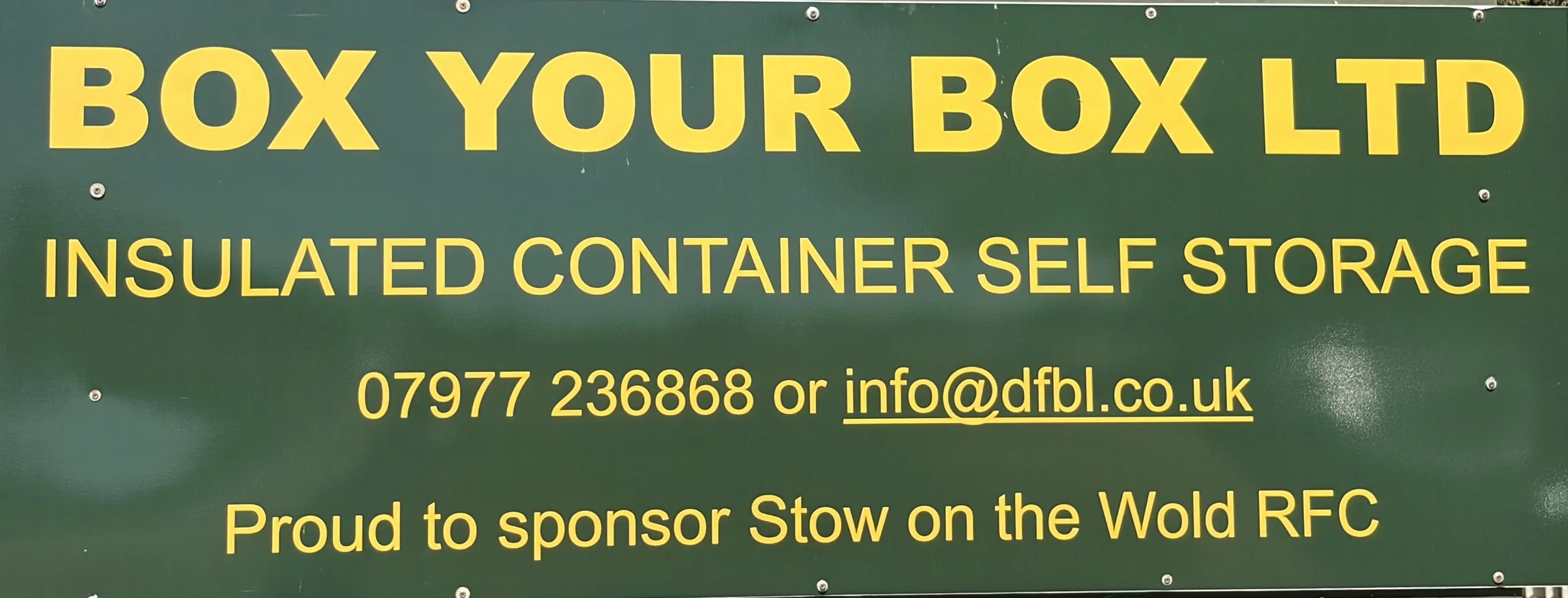 Green sign with yellow text advertising insulated container self-storage, providing a phone number, email address, and sponsorship information for Stow on the Wold RFC.