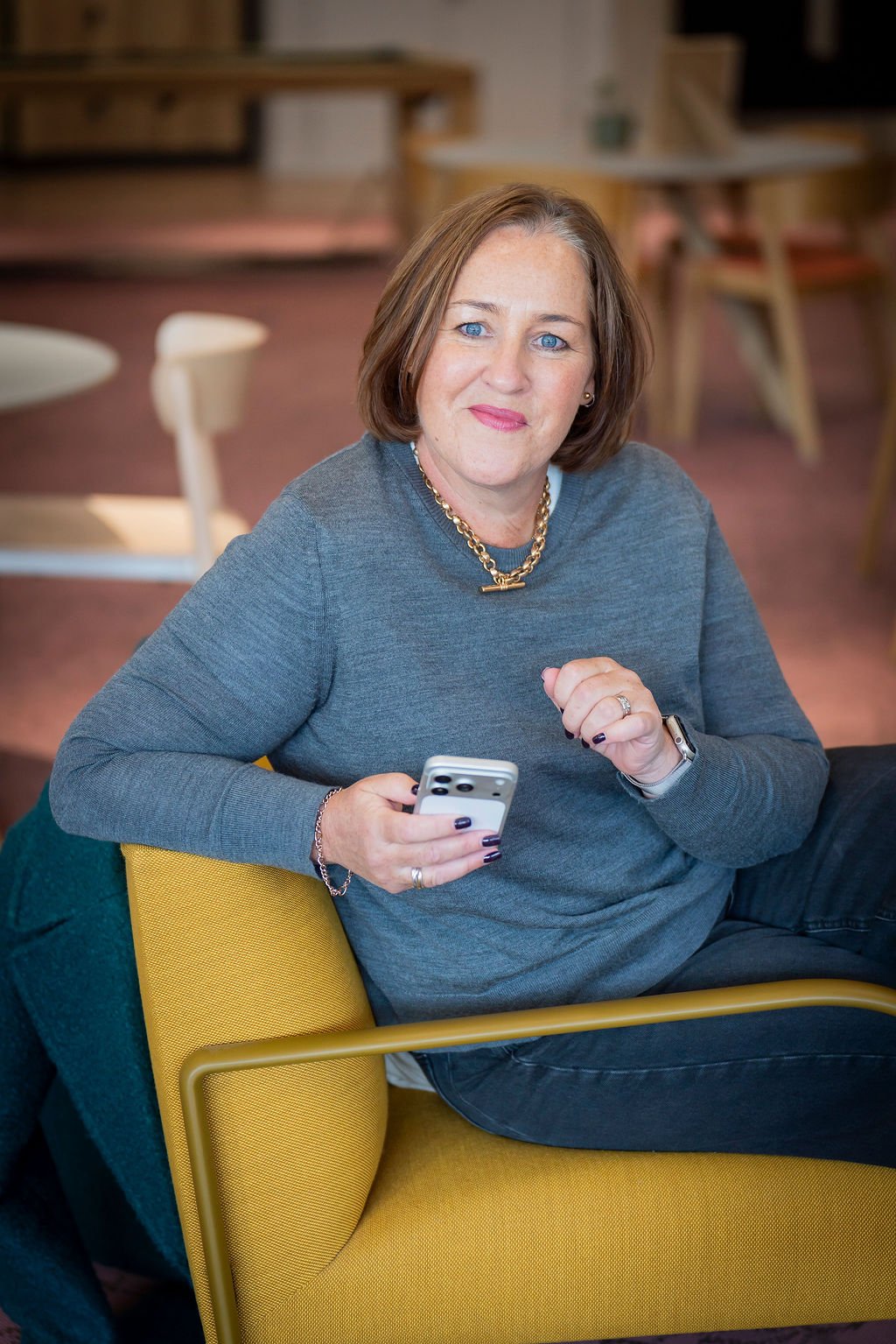Tech recruitment specialist sitting in yellow chair holding mobile phone