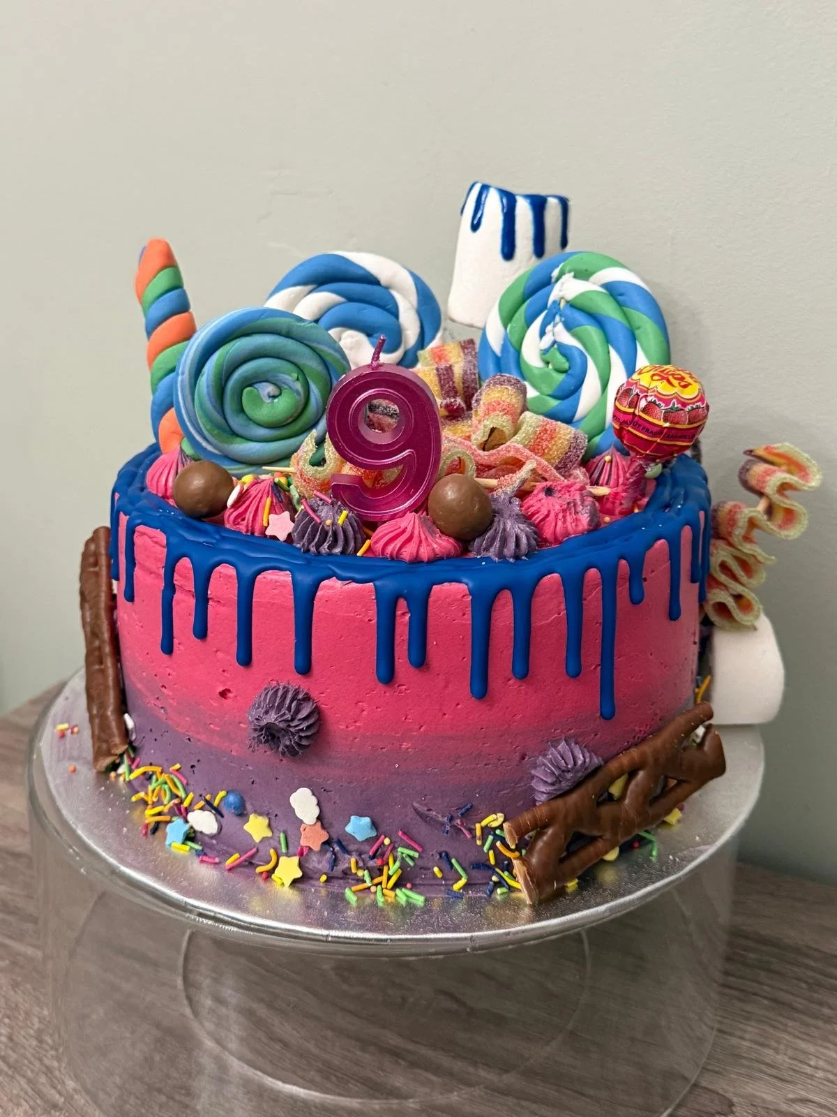 Pink and blue sweet-shop drip birthday cake with lollipops and doughnuts