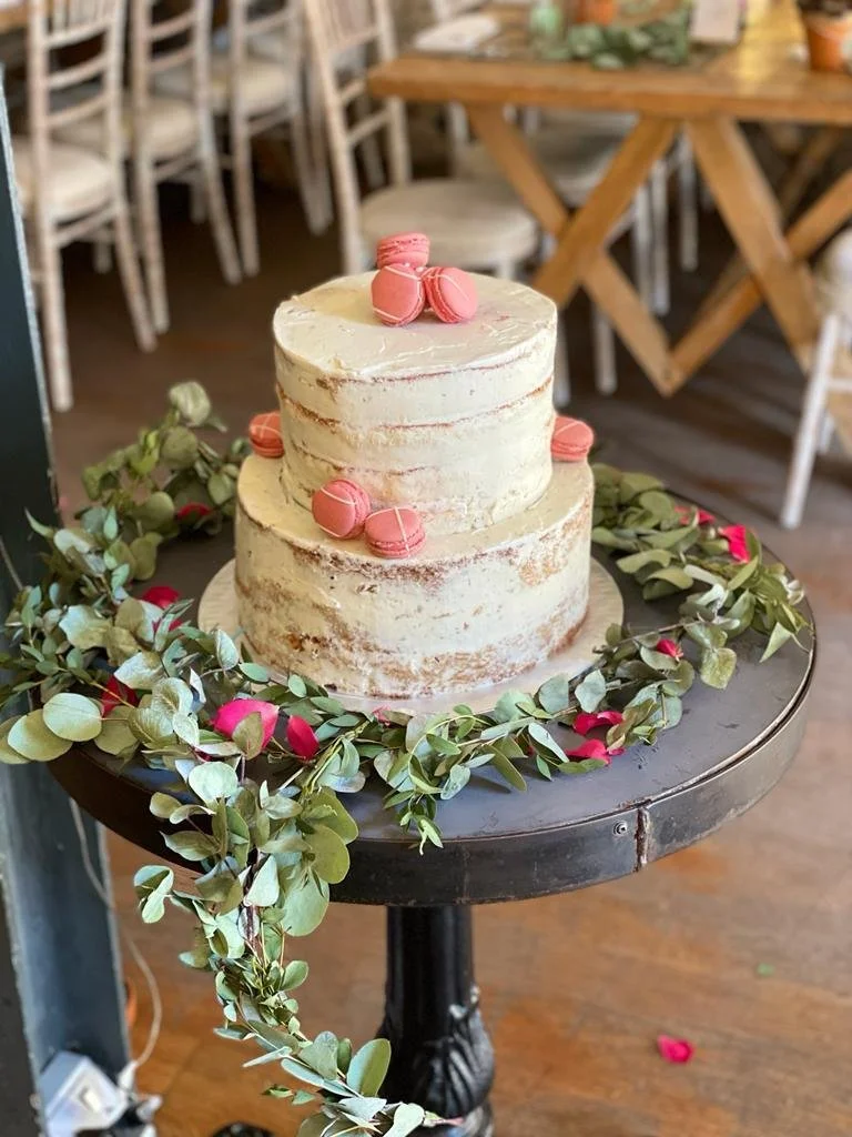 Two-tier semi-naked wedding cake with pink macarons and eucalyptus