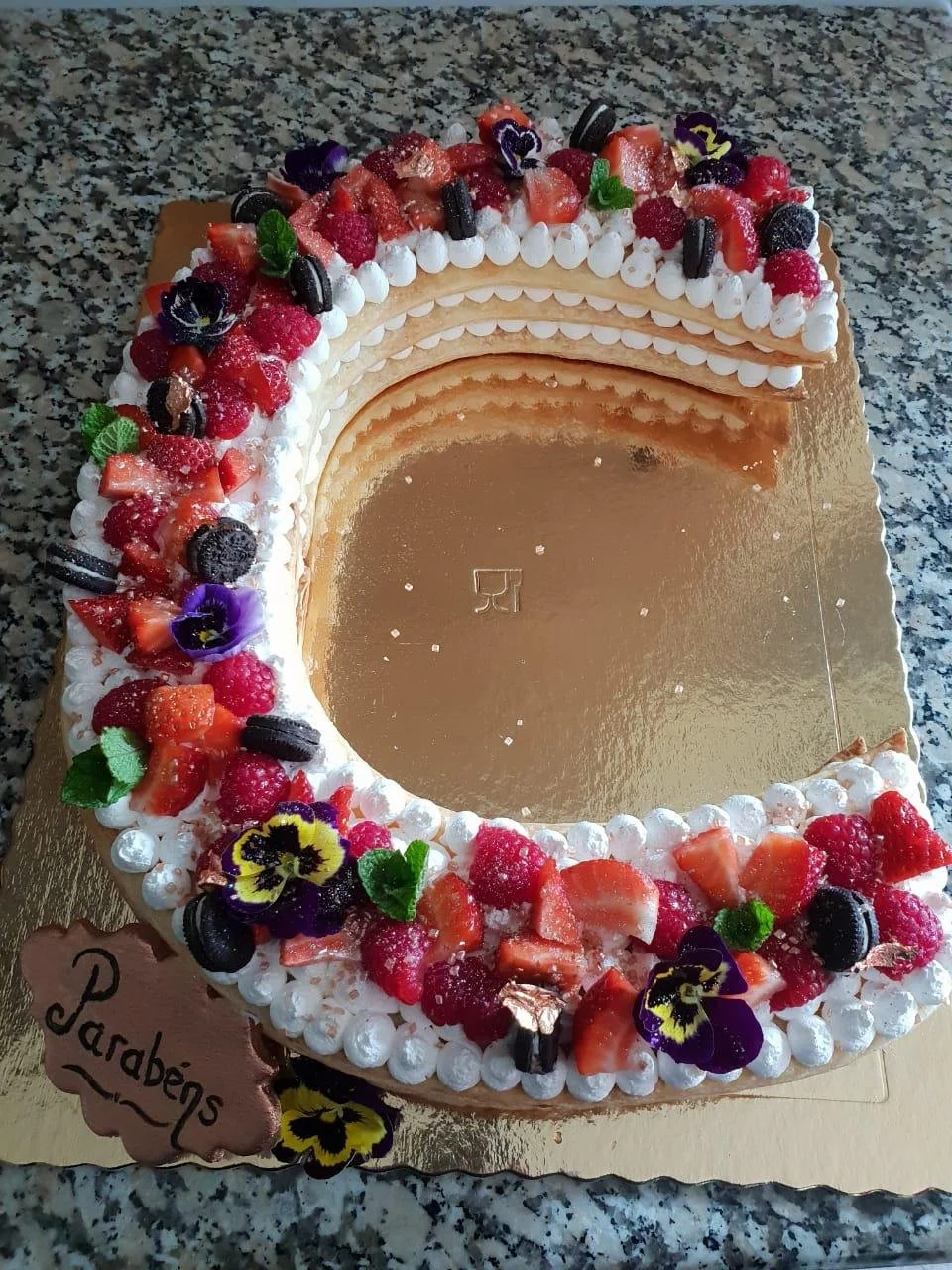 Letter-shaped celebration cake decorated with fresh berries and flowers