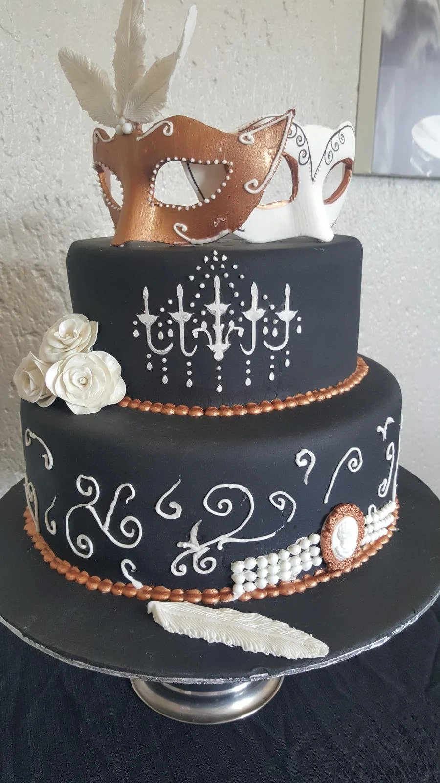 Two-tier black and gold masquerade cake with mask and feathers