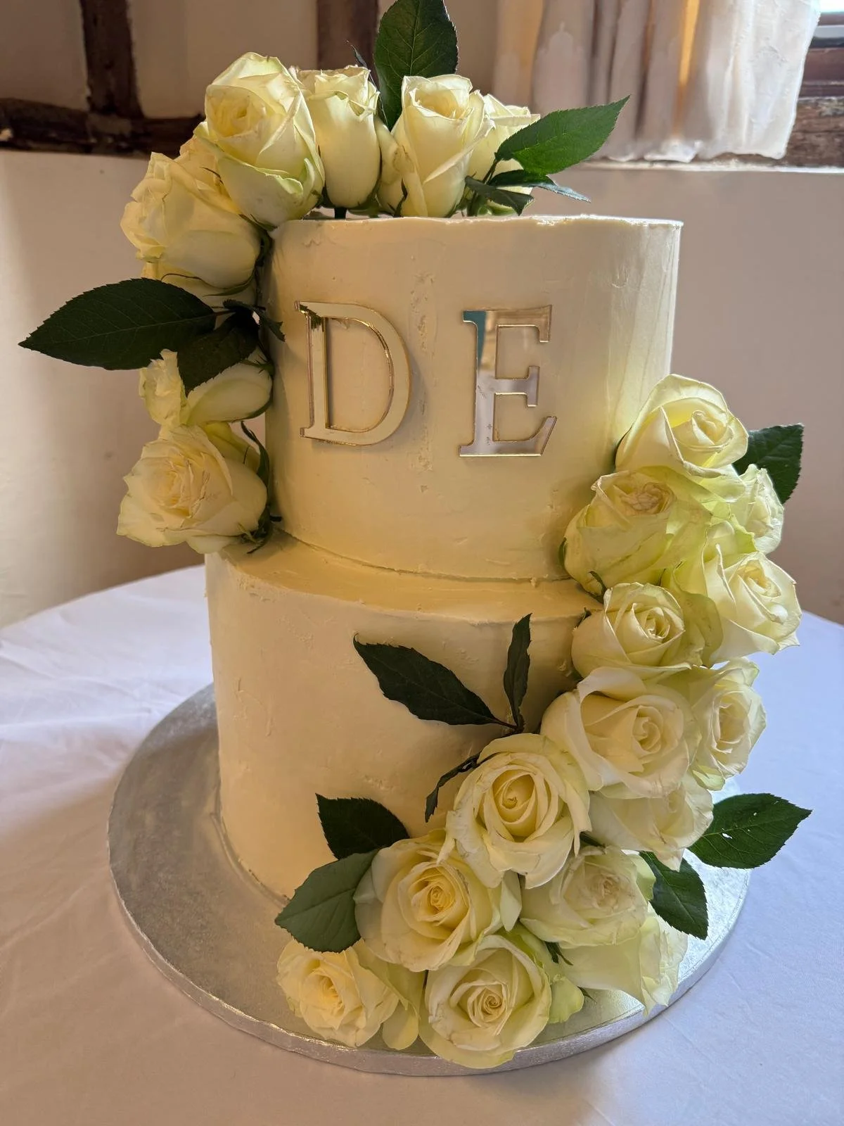 Two-tier wedding cake with cream roses and a gold monogram