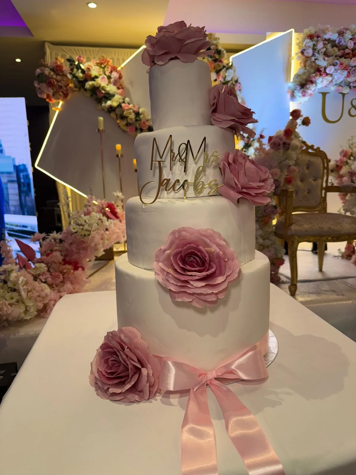 Four-tier white wedding cake with dusky pink sugar roses and a gold Mr & Mrs topper