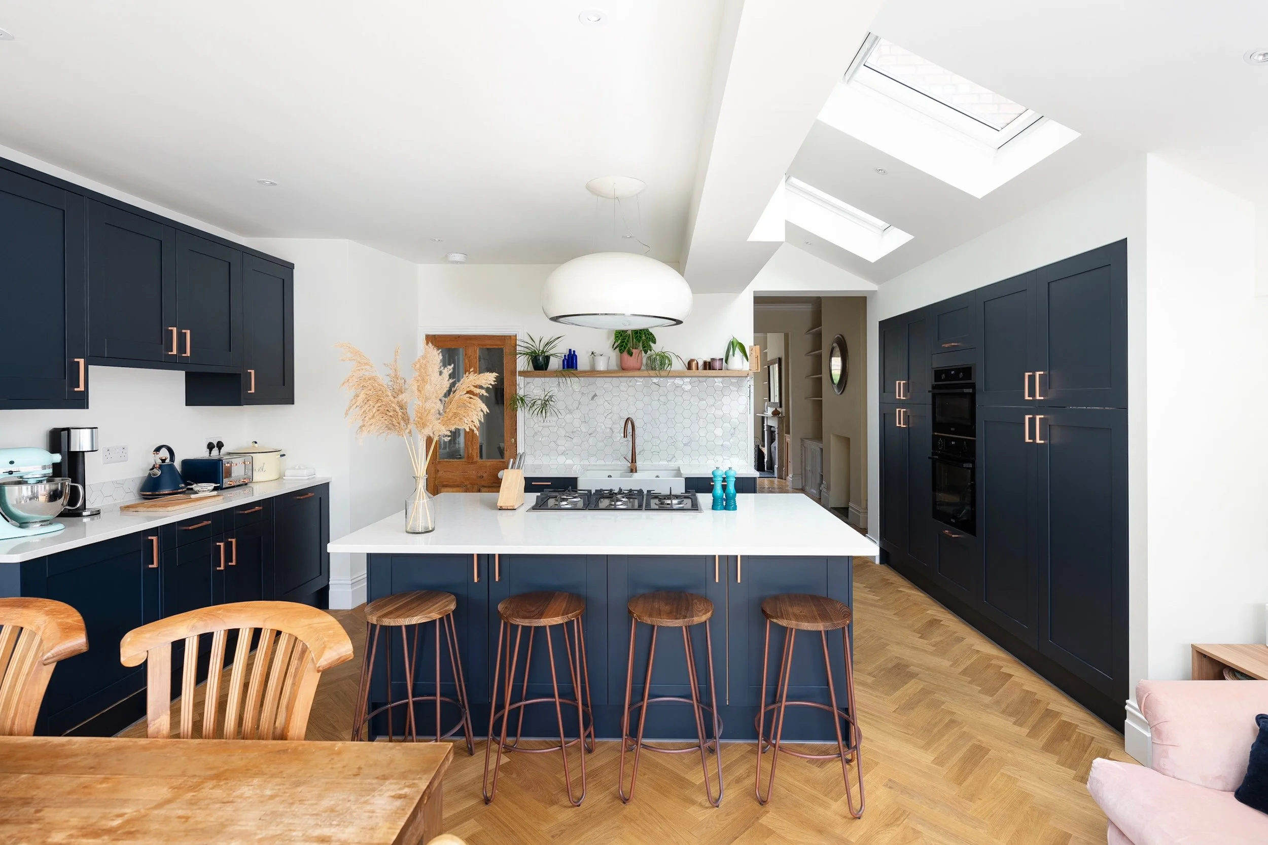 Navy shaker kitchen with a central island and bar stools beneath roof lights, opening through to the original living room , in Bishopston by JG Build.