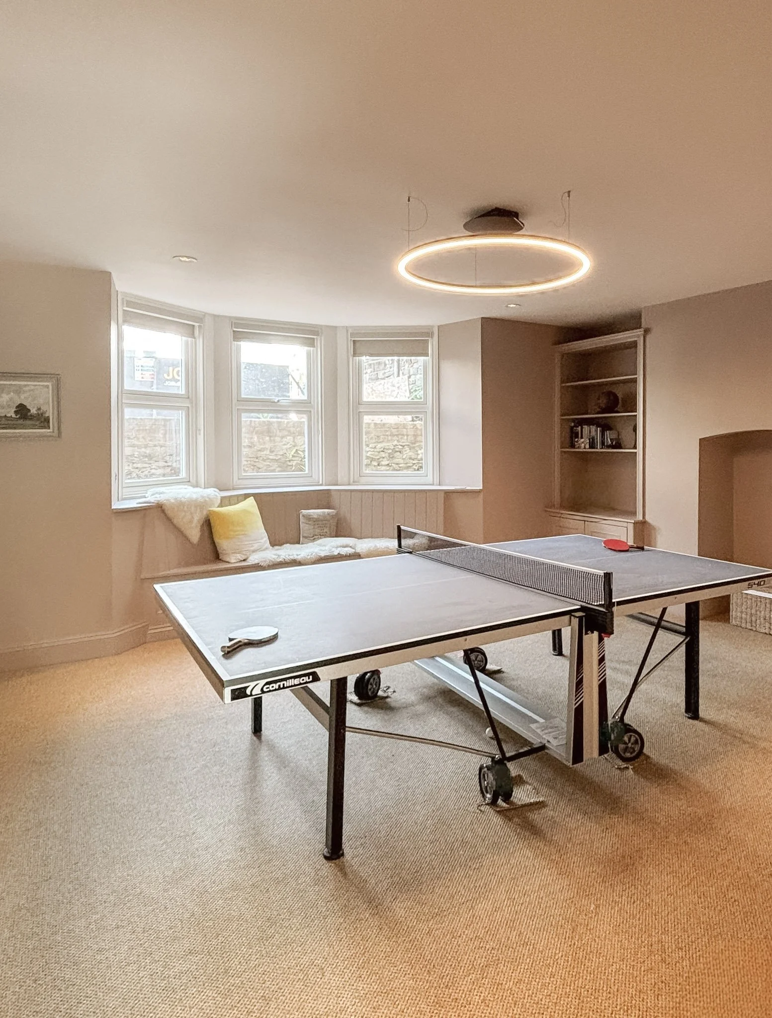 Basement games room with a bay window seat, built-in shelving and a circular pendant light, in Clifton by JG Build.