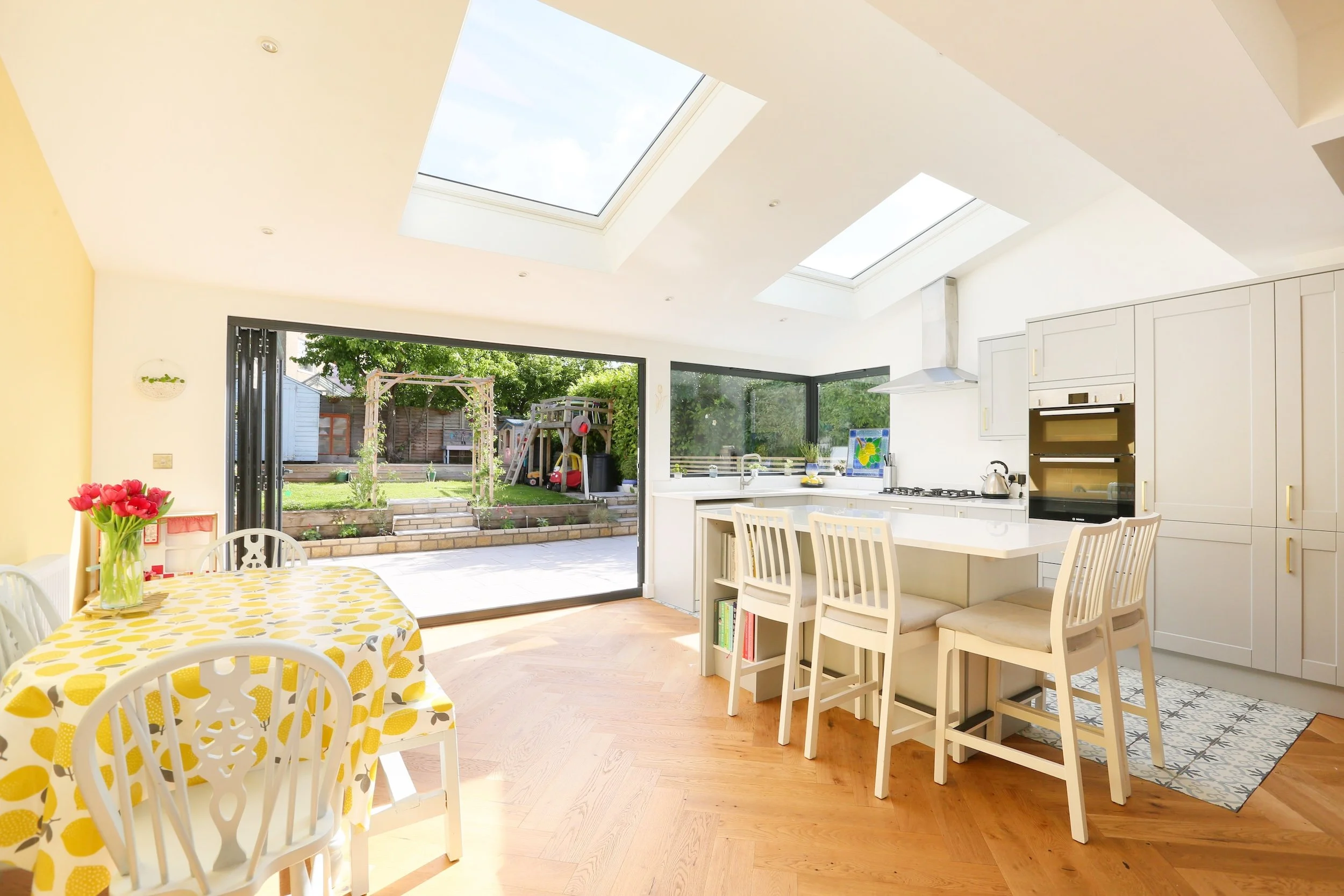Rear kitchen extension with roof lights, bi-fold doors and a corner window onto the garden, with a pale grey shaker kitchen, island and herringbone wood flooring, in Bristol by JG Build.