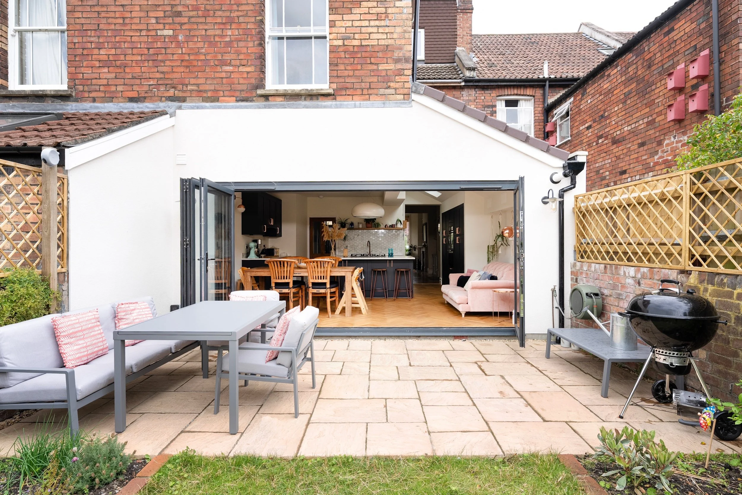 Rendered rear extension with bi-fold doors open onto a stone patio, showing the kitchen and living space inside, on a period terrace in Bishopston by JG Build.
