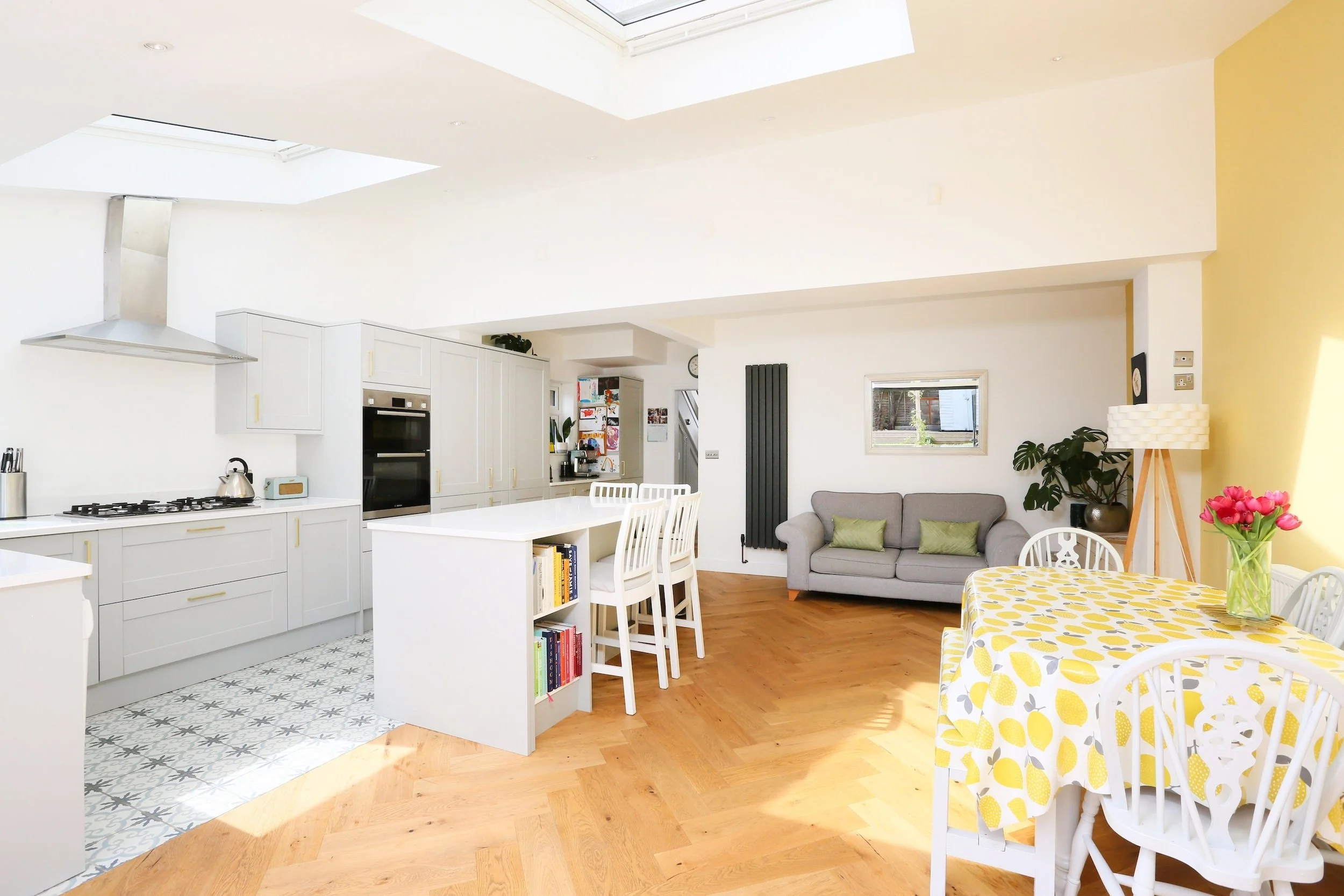 Open-plan kitchen, dining and living space with roof lights, a pale grey shaker kitchen and island, and herringbone wood flooring, in Bristol by JG Build.