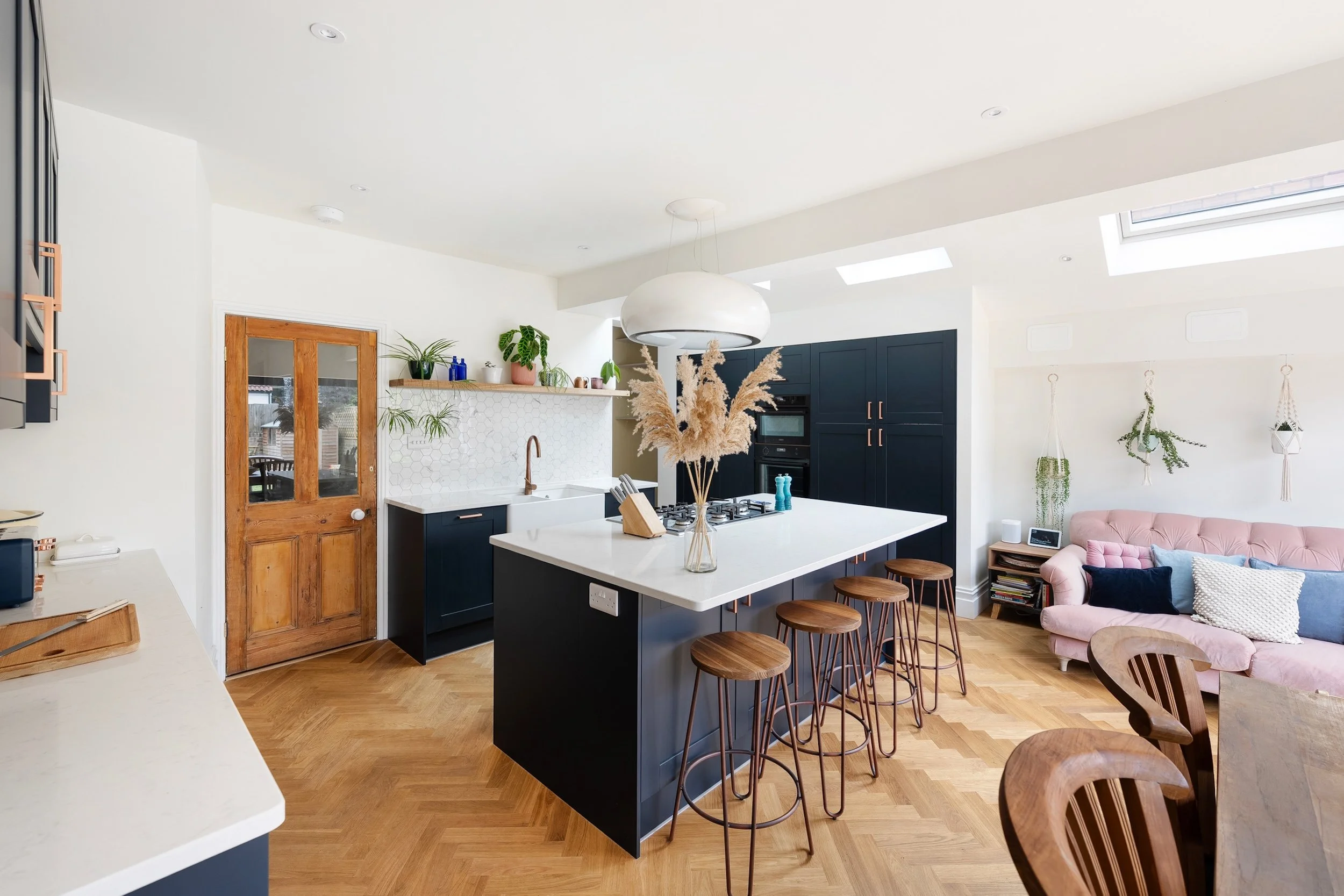 Open-plan kitchen and living space with a navy island and bar stools, oak herringbone flooring and roof lights, in Bishopston by JG Build.