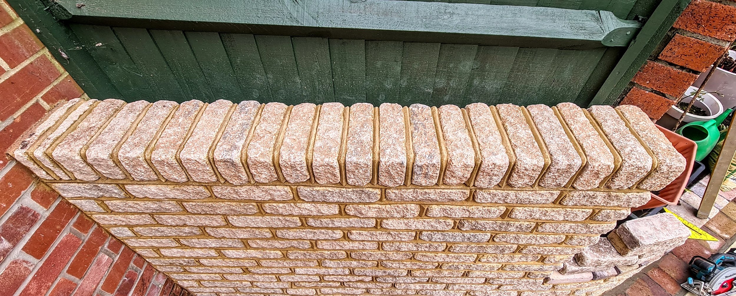 A row of light pink bricks with a rough textured surface stacked on top of a wall made of similar bricks.