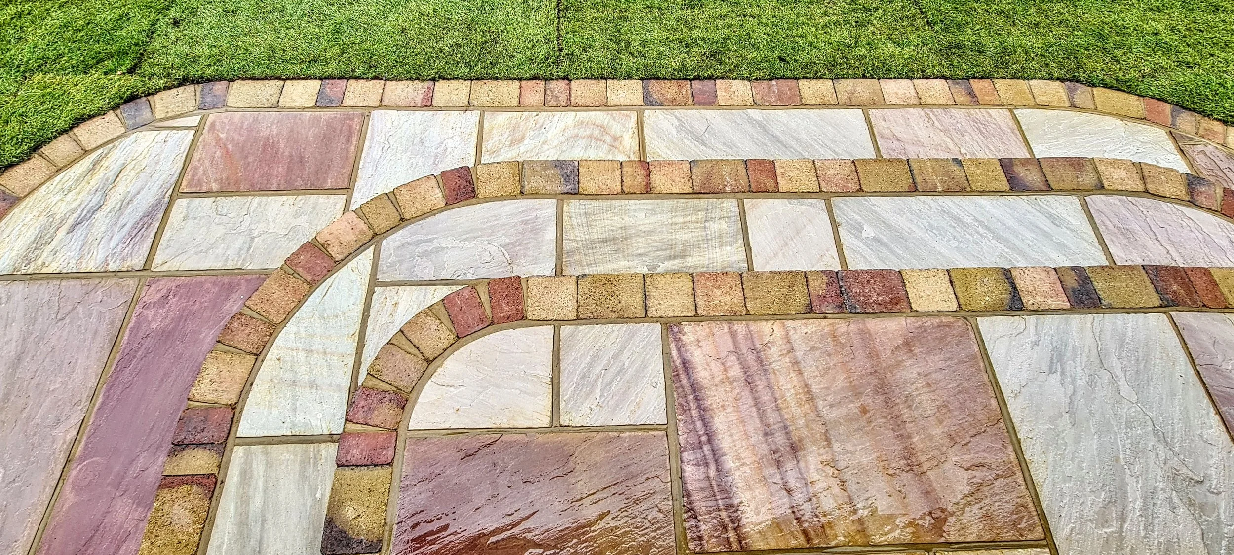 Decorative stone and brick pattern on sidewalk with a grass border.