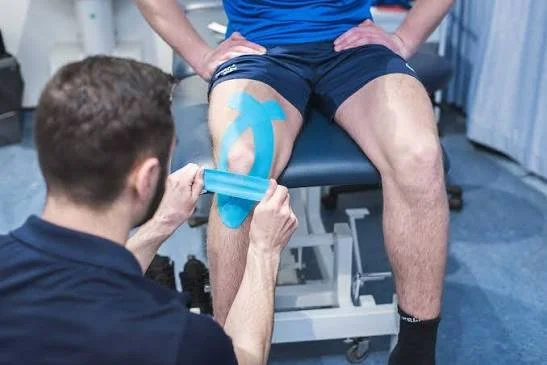 Physical therapist applying kinesiology tape to a patient's leg during a therapy session.
