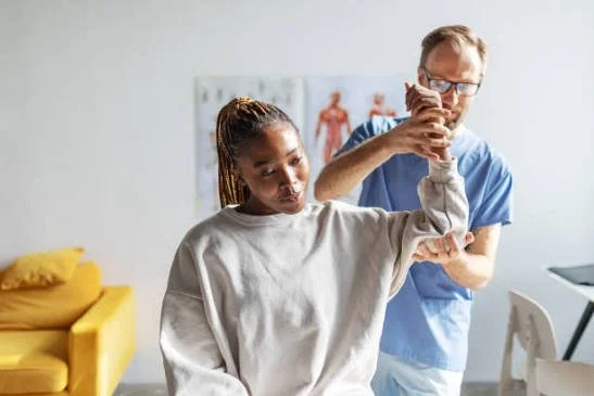 A healthcare professional holding a woman's arm in a medical setting with anatomical charts on the wall.