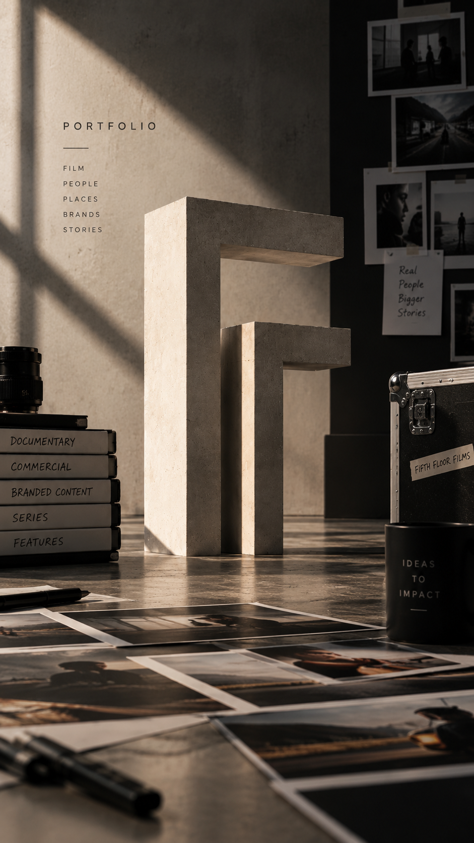 A photography or film portfolio workspace with concrete sculptures, photo prints, and files labeled for documentaries, commercial content, series, and features. Photographs are pinned on the wall, and sunlight creates shadows.