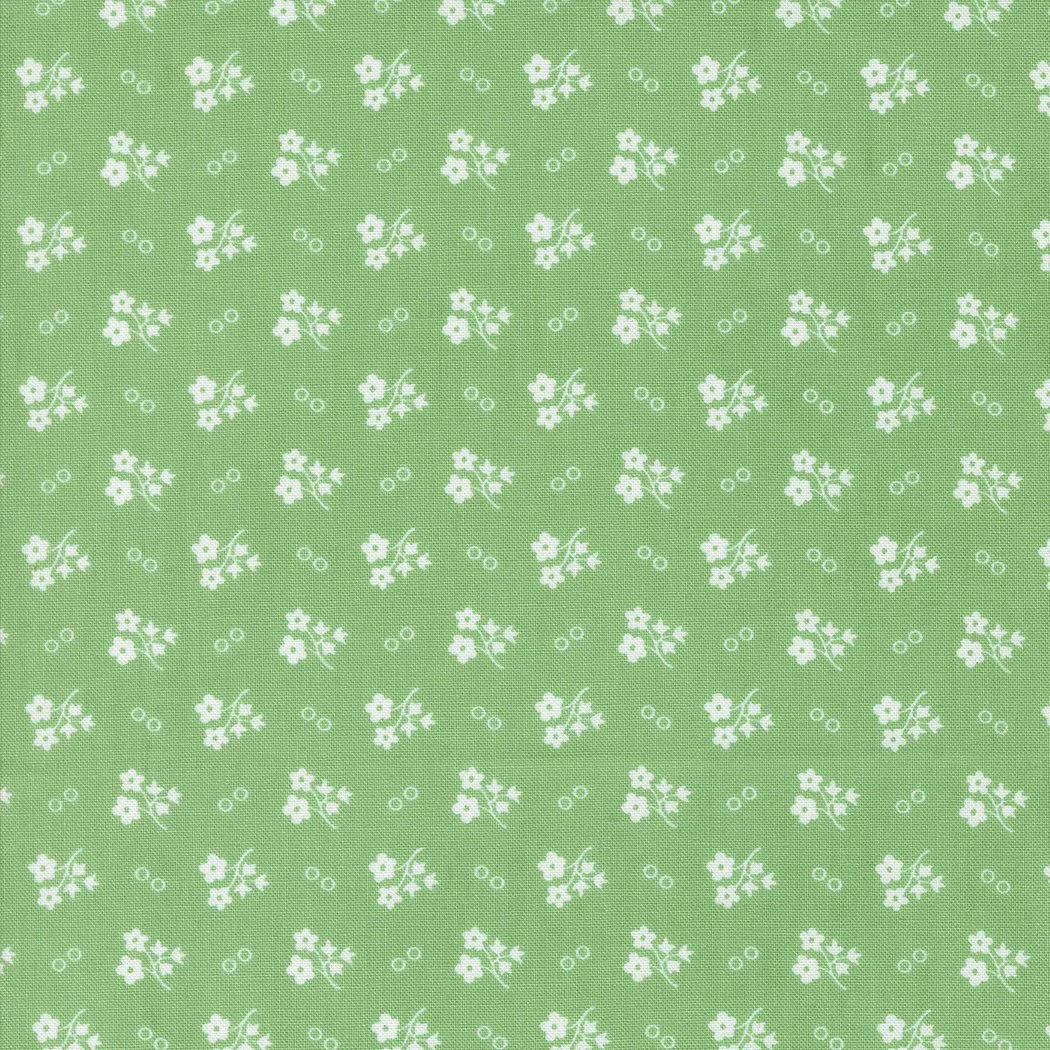 Green fabric with small white floral pattern and tiny circles scattered throughout.