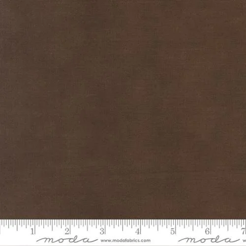 A close-up photograph of a plain brown fabric with a measuring tape at the bottom showing inches.