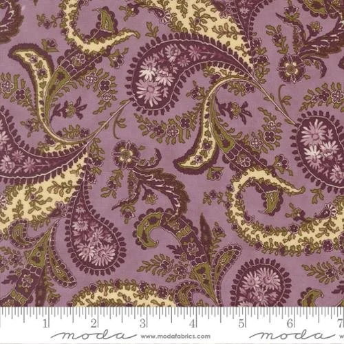 Close-up of a fabric with a purple background and a paisley floral pattern in shades of purple, green, and gold, with a measuring ruler at the bottom.