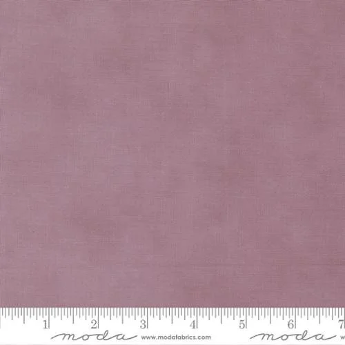 A close-up of pink fabric with a measurement ruler at the bottom, labeled 'moda fabrics'.
