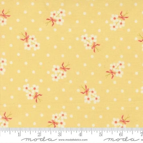 Yellow fabric with small white and pink floral pattern and red bows, with a ruler at the bottom showing inches.