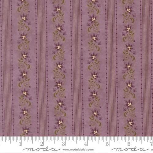 Close-up of purple fabric with vertical gold and purple floral patterns and small gold dots, with a ruler showing measurements in inches at the bottom.