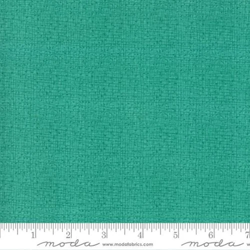 Close-up of green fabric with a ruler at the bottom showing measurement in inches.