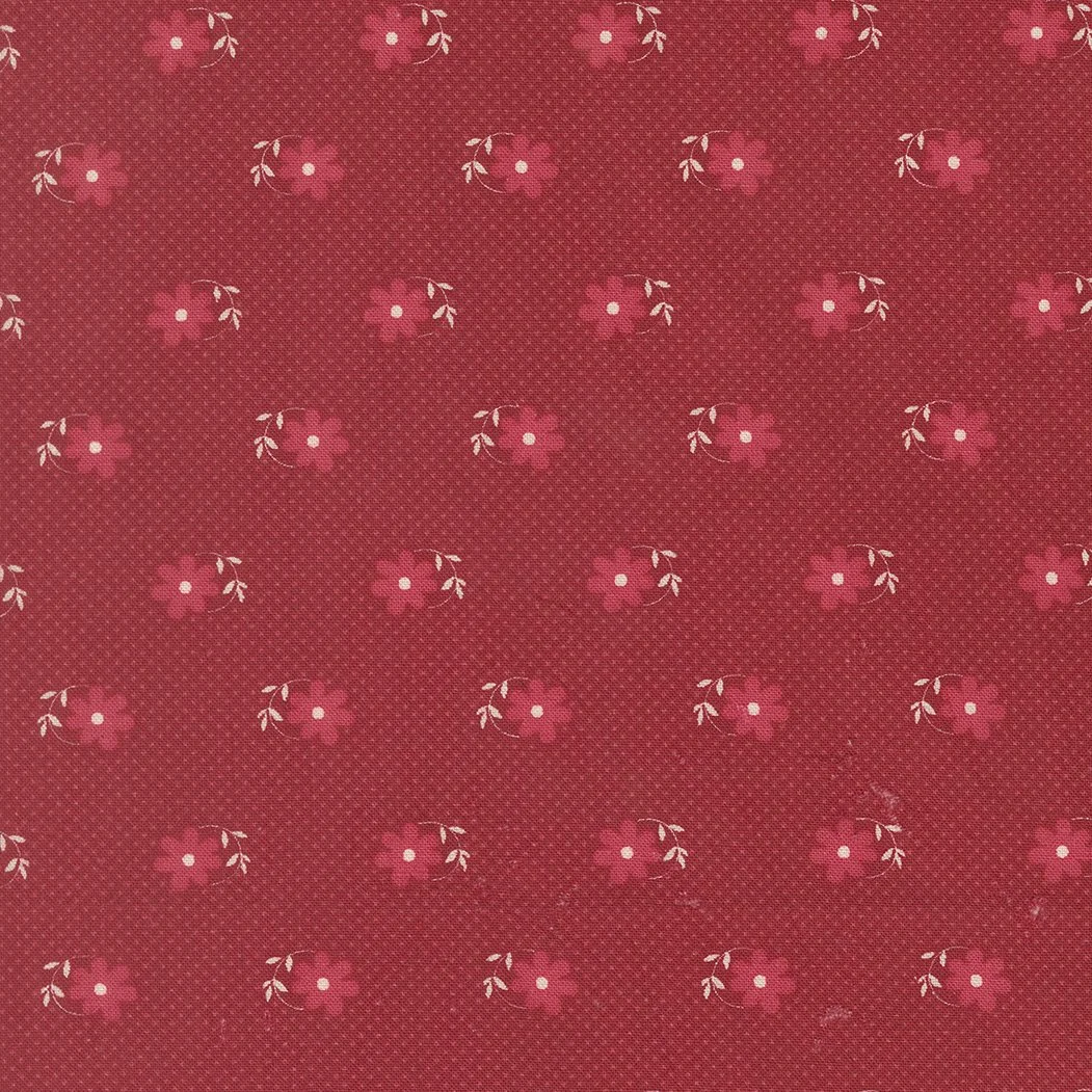 Red fabric with small pink flowers and white leaves arranged in a repeating pattern.