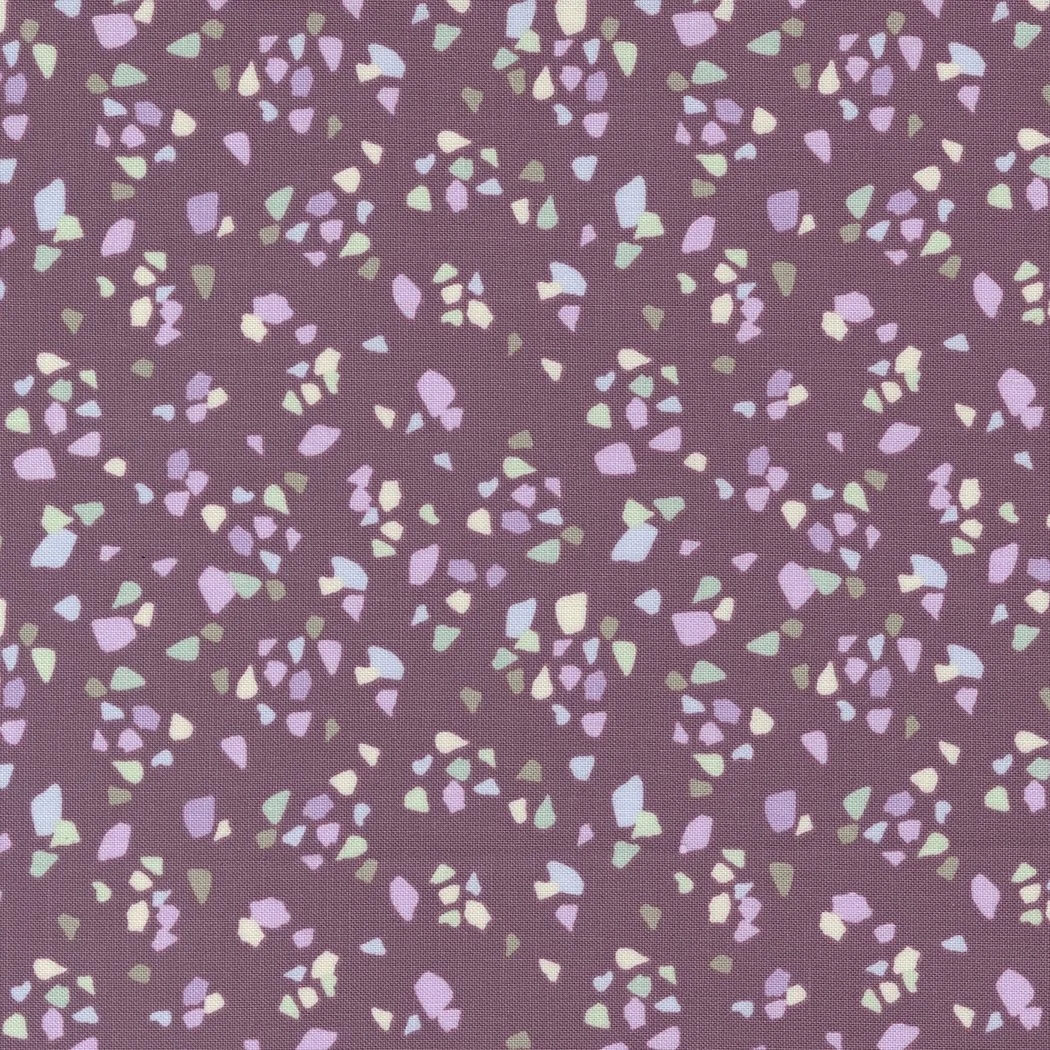A fabric pattern with small, irregularly shaped confetti-like spots in pastel colors on a mauve background.