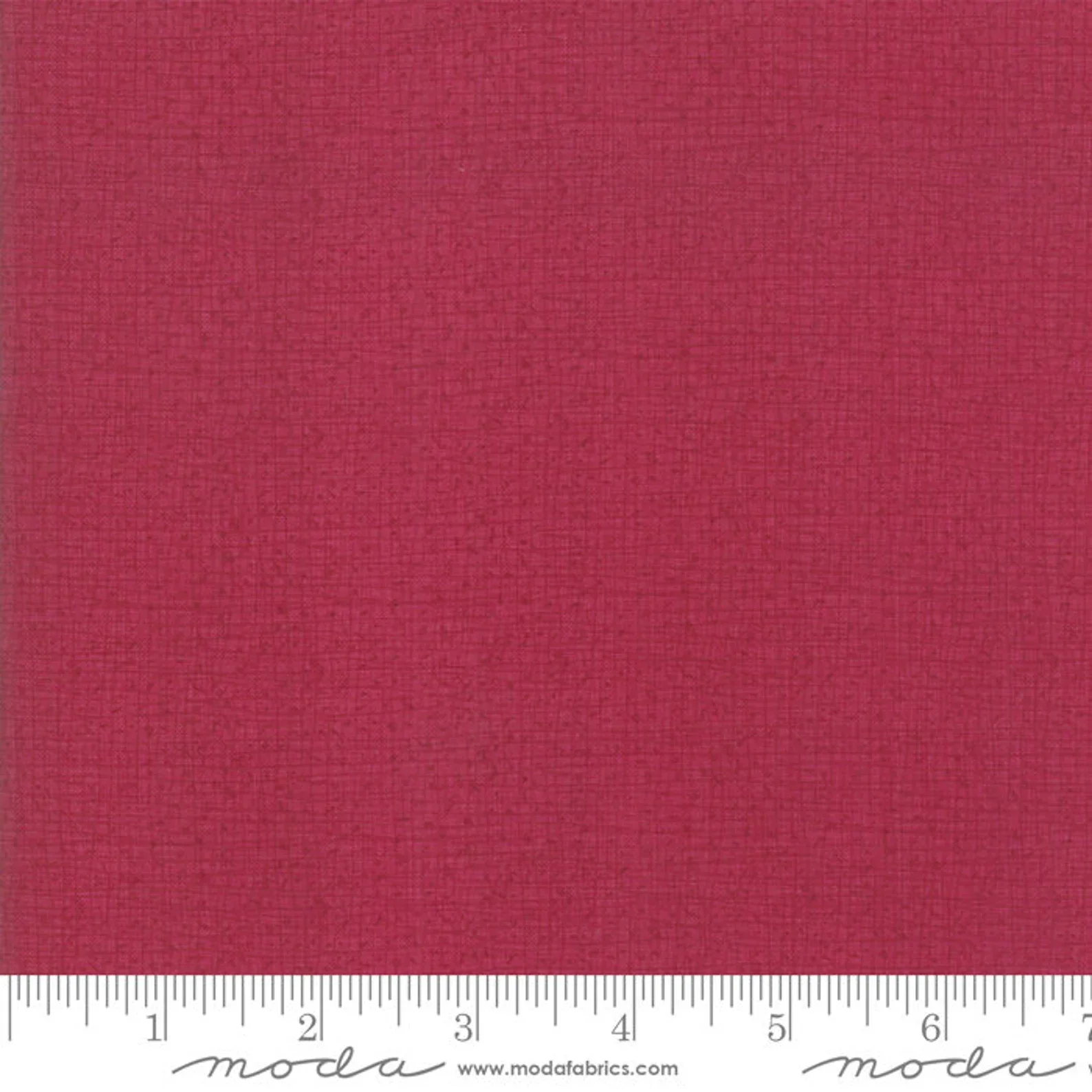 A close-up view of red textured fabric with a ruler at the bottom showing inches, and the 'moda' logo on the fabric branding. 