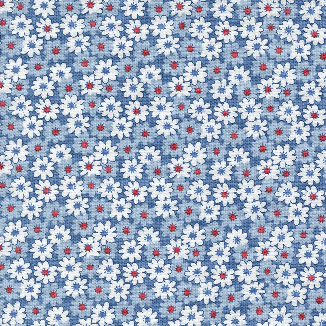 Close-up of a fabric with a pattern of white flowers with five petals, red centers, and small light blue flowers on a blue background.