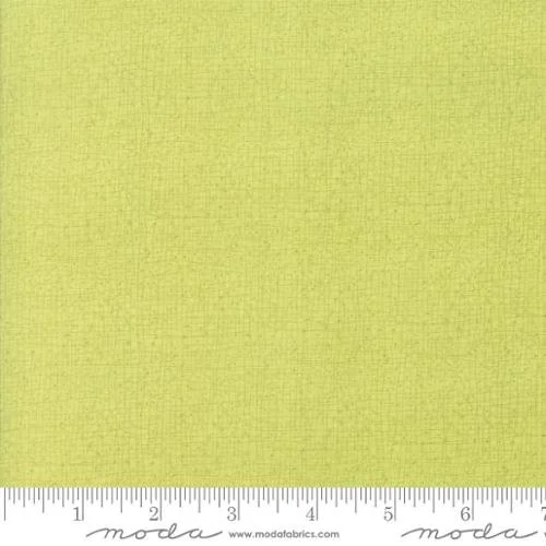 Close-up of a lime green fabric with a subtle textured weave and a measuring ruler at the bottom showing inches.