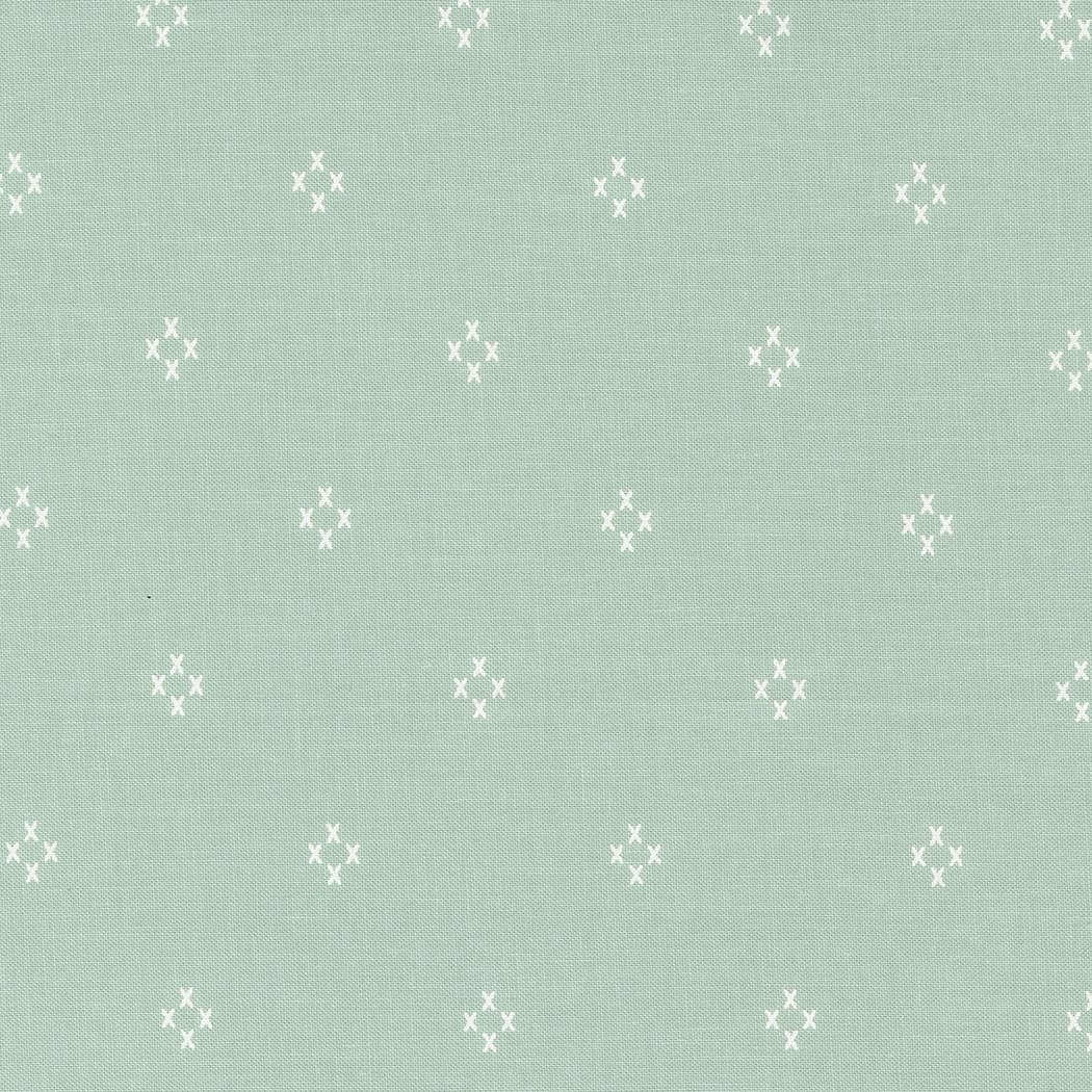 A close-up of a light turquoise fabric with a small repeating pattern of white dots arranged in a floral or star-like formation.
