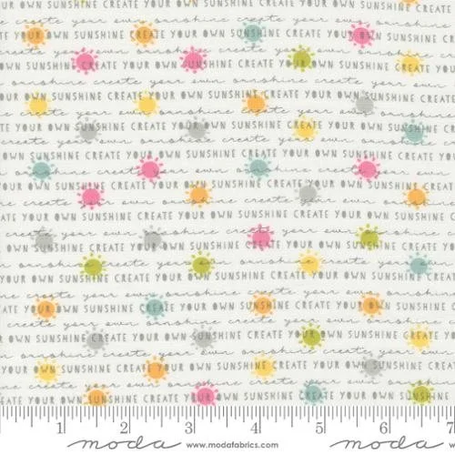 Close-up of fabric with a repeating pattern of the phrase "Create your own sunshine" and small colorful abstract shapes in pink, yellow, orange, and teal, with a ruler at the bottom for scale.